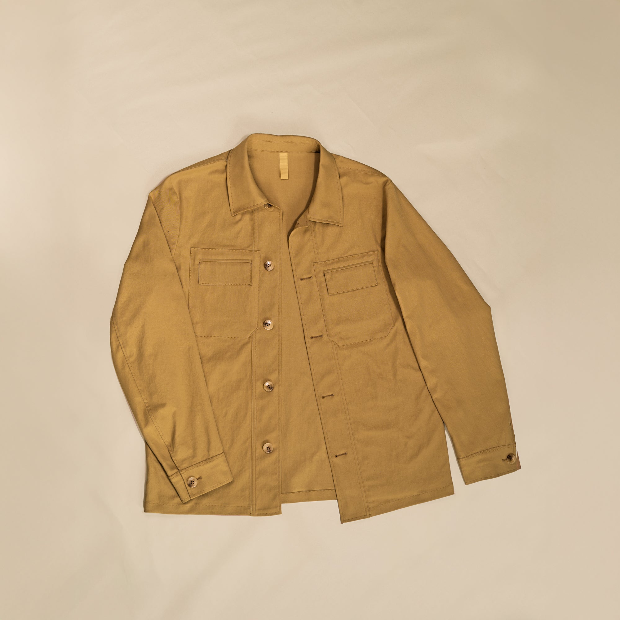Flat lay of the WJ-001 work jacket in tan, featuring a button front, two chest flap pockets, and cuffed sleeves.